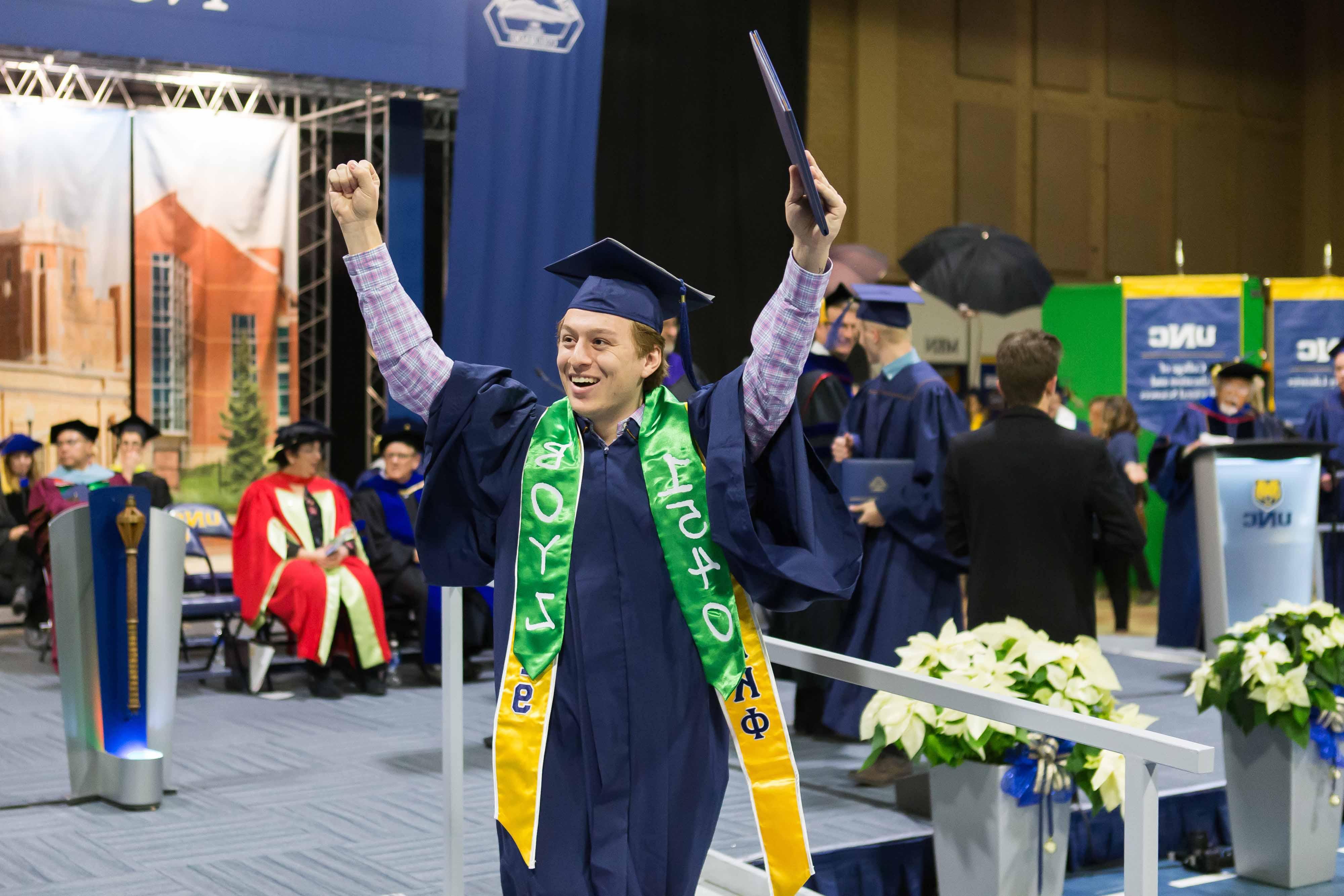 Student holds their diploma above their head.